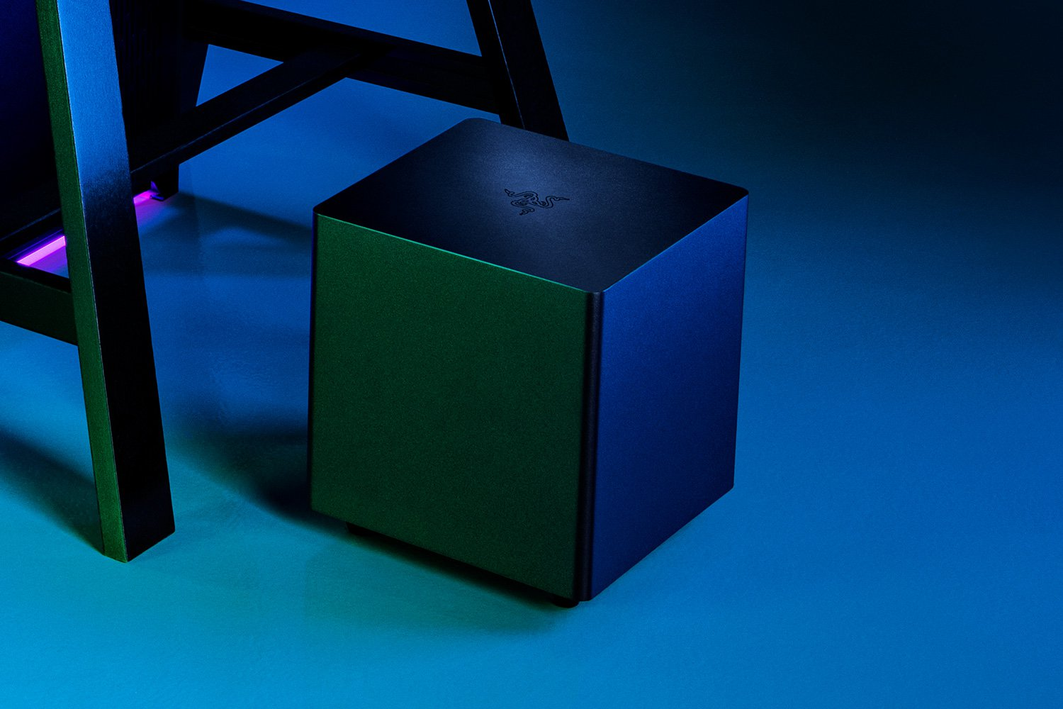 Zwarte Razer subwoofer kubus geplaatst op een blauw gradiënt oppervlak, nabij een zwart statief.