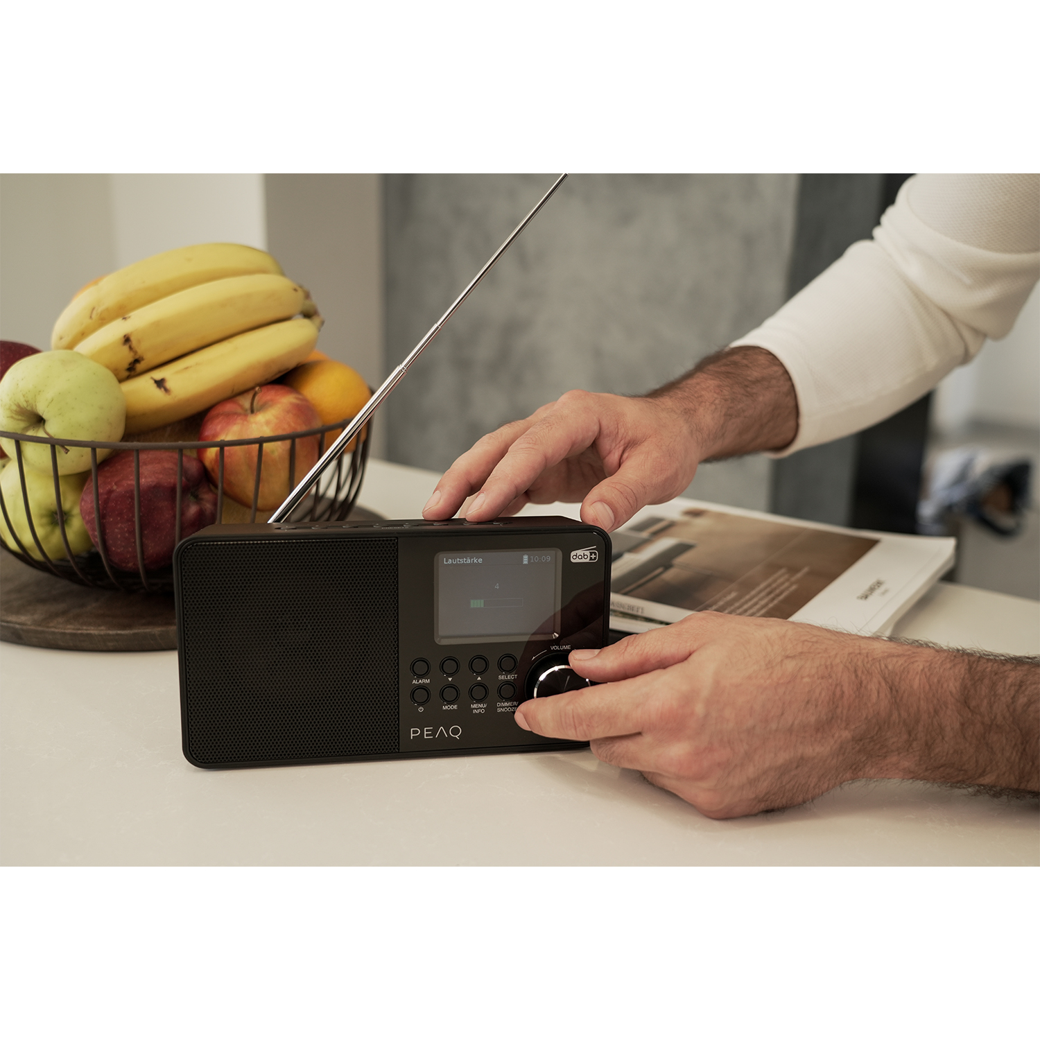 Mani che azionano una radio nera con display. Accanto una fruttiera.