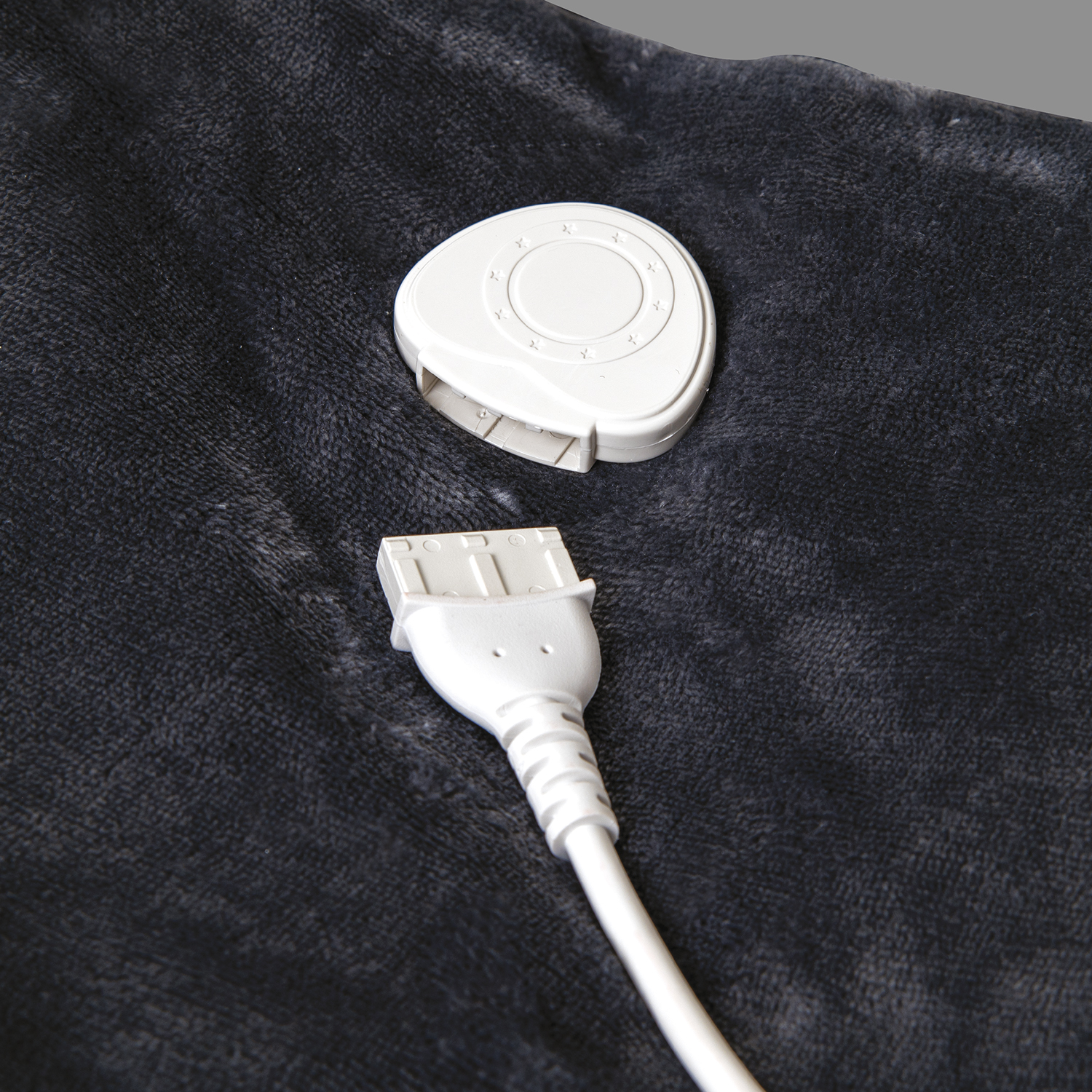 Adattatore di alimentazione bianco collegato a una coperta grigio scuro. Connettore visibile. Primo piano.