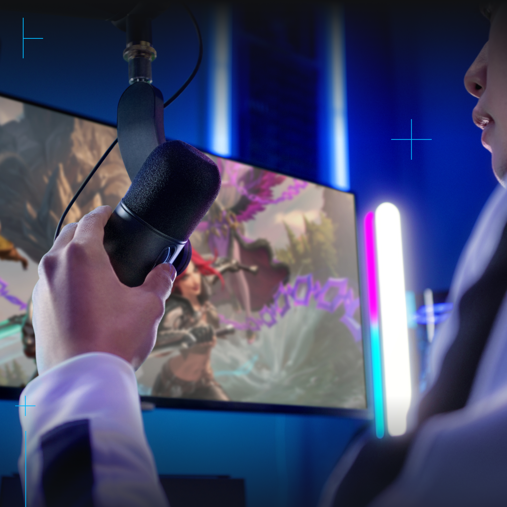Una persona sosteniendo un micrófono negro frente a una pantalla de computadora con una escena de juego y luces coloridas.