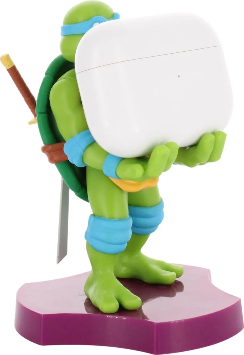 Tortue Ninja tenant un étui d'écouteurs blanc. Épée marron sur le dos, figurine verte, socle violet.