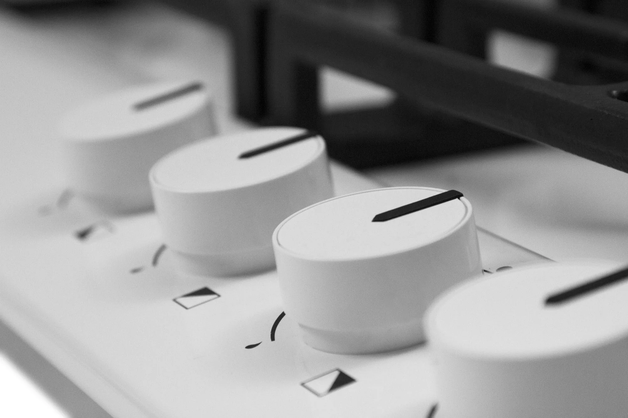 Białe pokrętła kuchenki z czarnymi wskaźnikami.