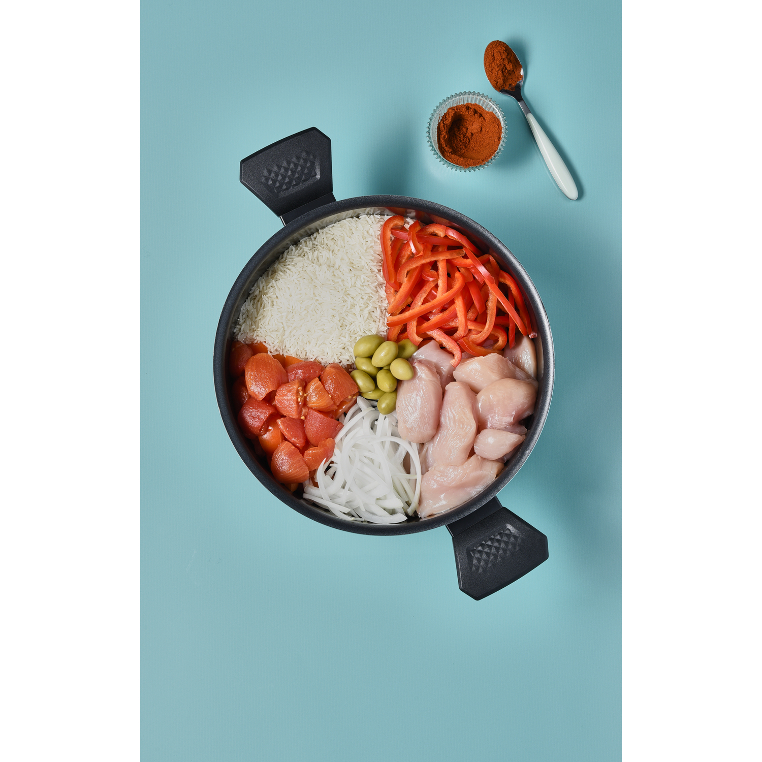 Ingredients arranged in a pan: rice, red pepper, chicken, etc., on blue surface.