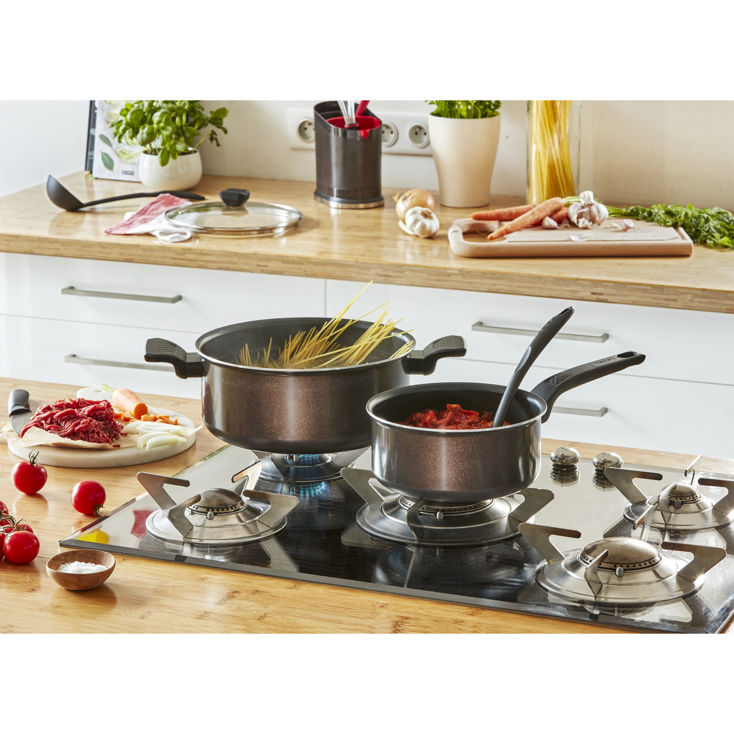 A kitchen scene with pots on a gas stove, vegetables, and a cutting board. A wooden surface.