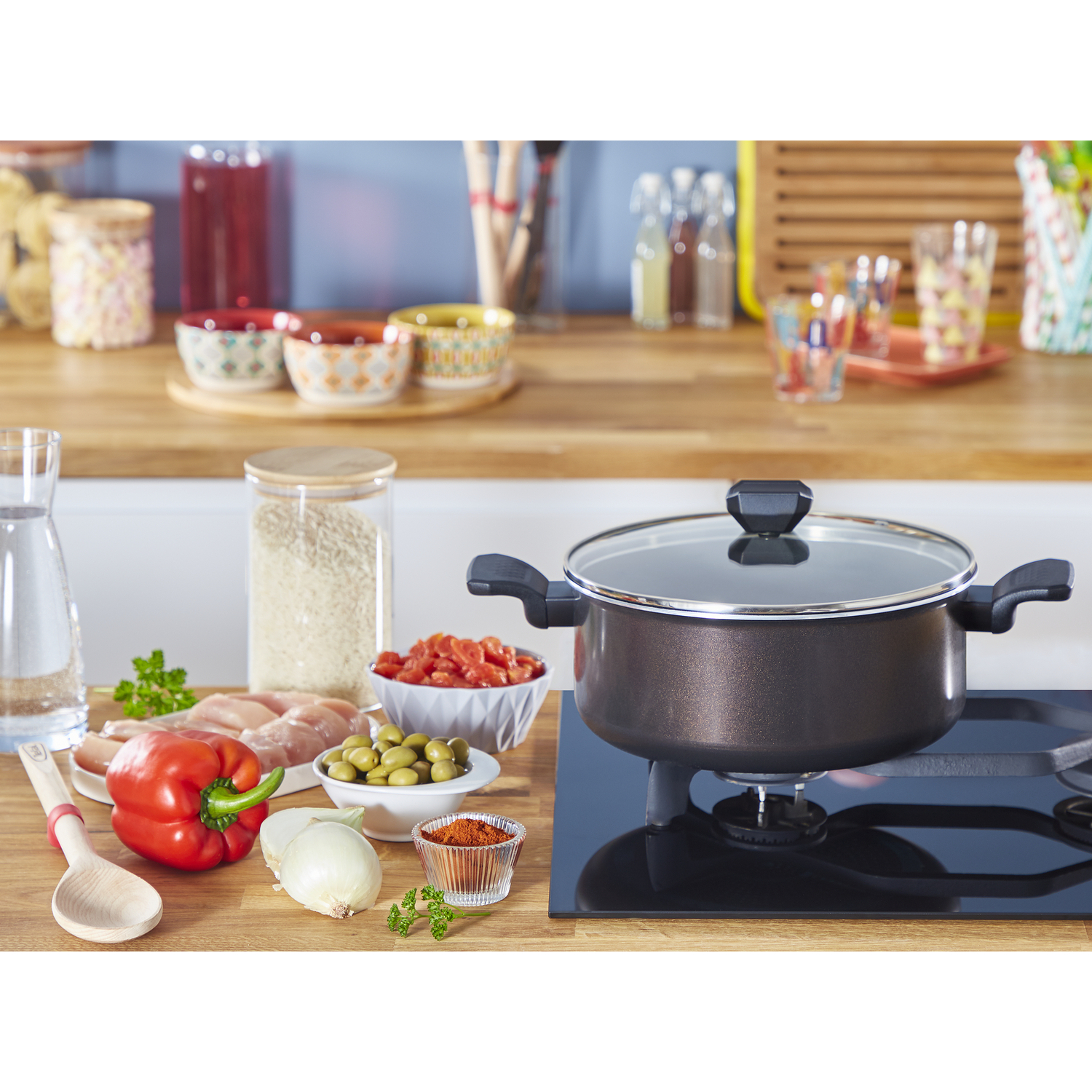 Kitchen scene with ingredients on a wooden counter and a pot on a stove. Includes red pepper and rice.