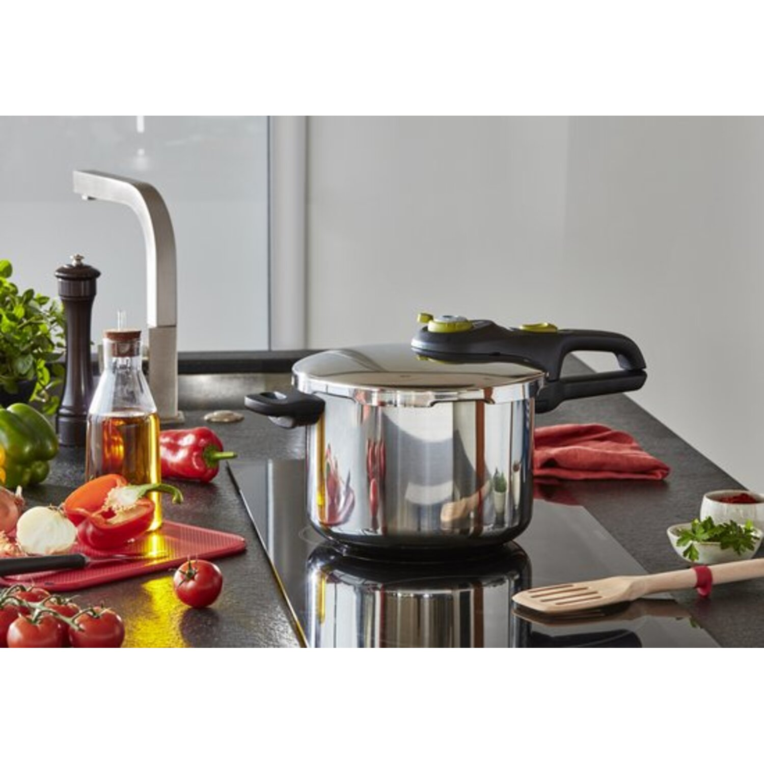 Stainless steel pressure cooker on a stovetop with vegetables and kitchenware.