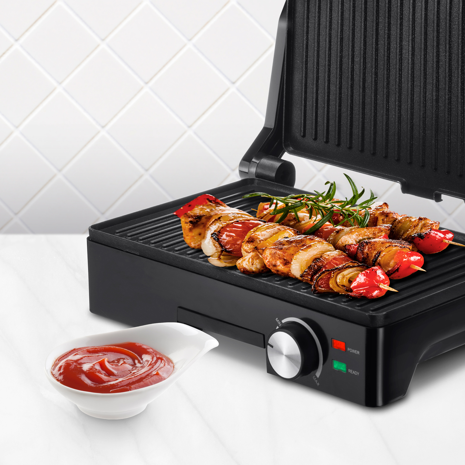 Parrilla negra con brochetas a la parrilla, un cuenco de ketchup y fondo de azulejos blancos.