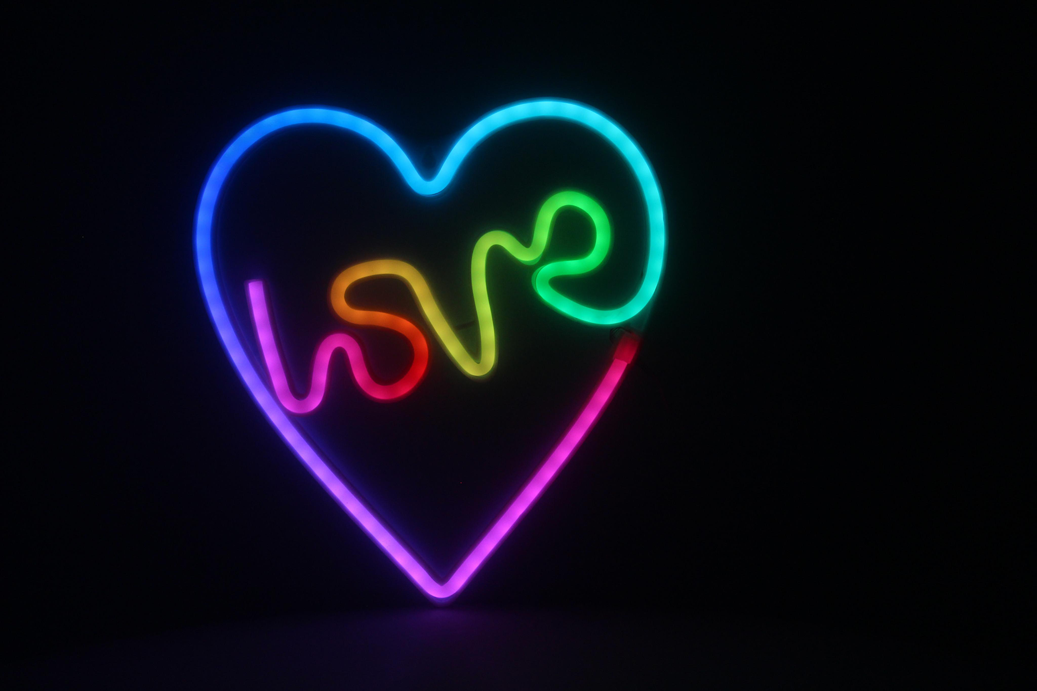 Neon szív alak, benne a 'love' felirattal, fekete háttér előtt világít.
