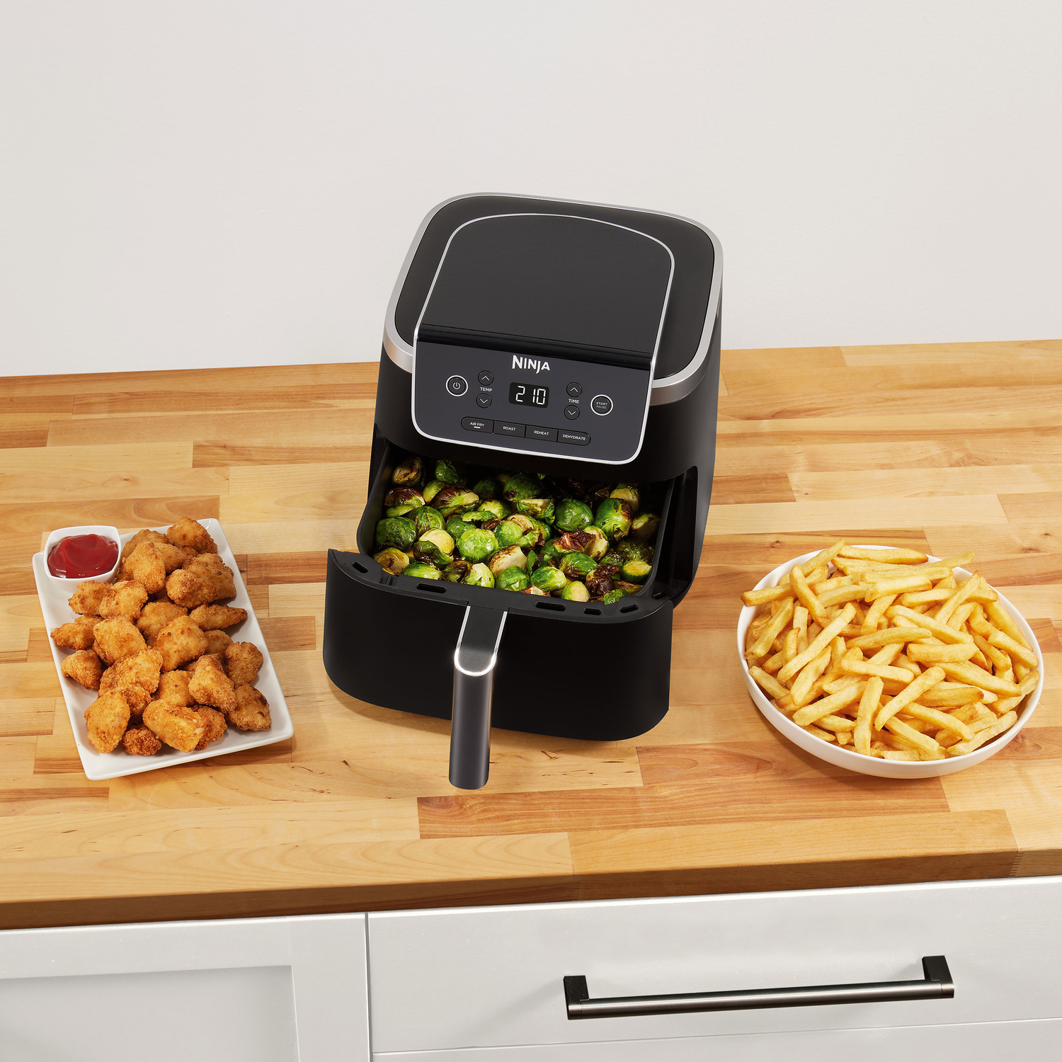 Een airfryer met gefrituurd voedsel, nuggets en friet op een houten oppervlak.