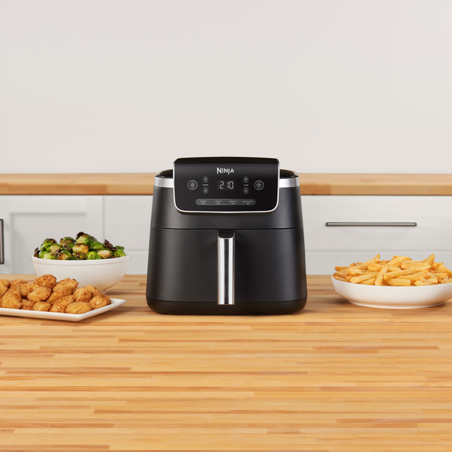 Zwarte airfryer met eten aan beide kanten. Inclusief gebakken kip, spruitjes en frietjes.