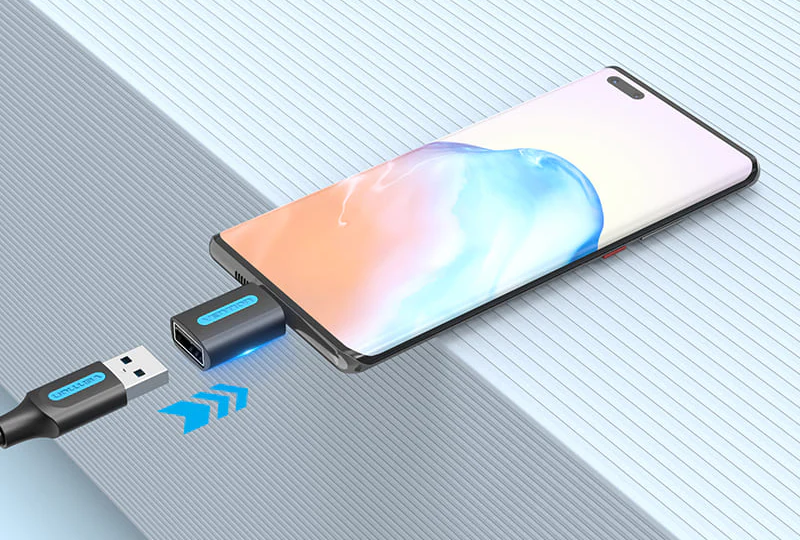 Okostelefon egy adapterhez és egy USB-kábelhez csatlakoztatva. Világoskék háttér.