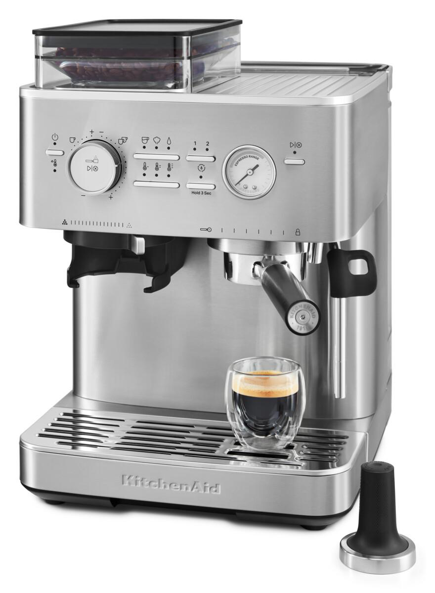 Edelstahl-Espressomaschine mit einem Glas Kaffee. Ein Tamper steht daneben.