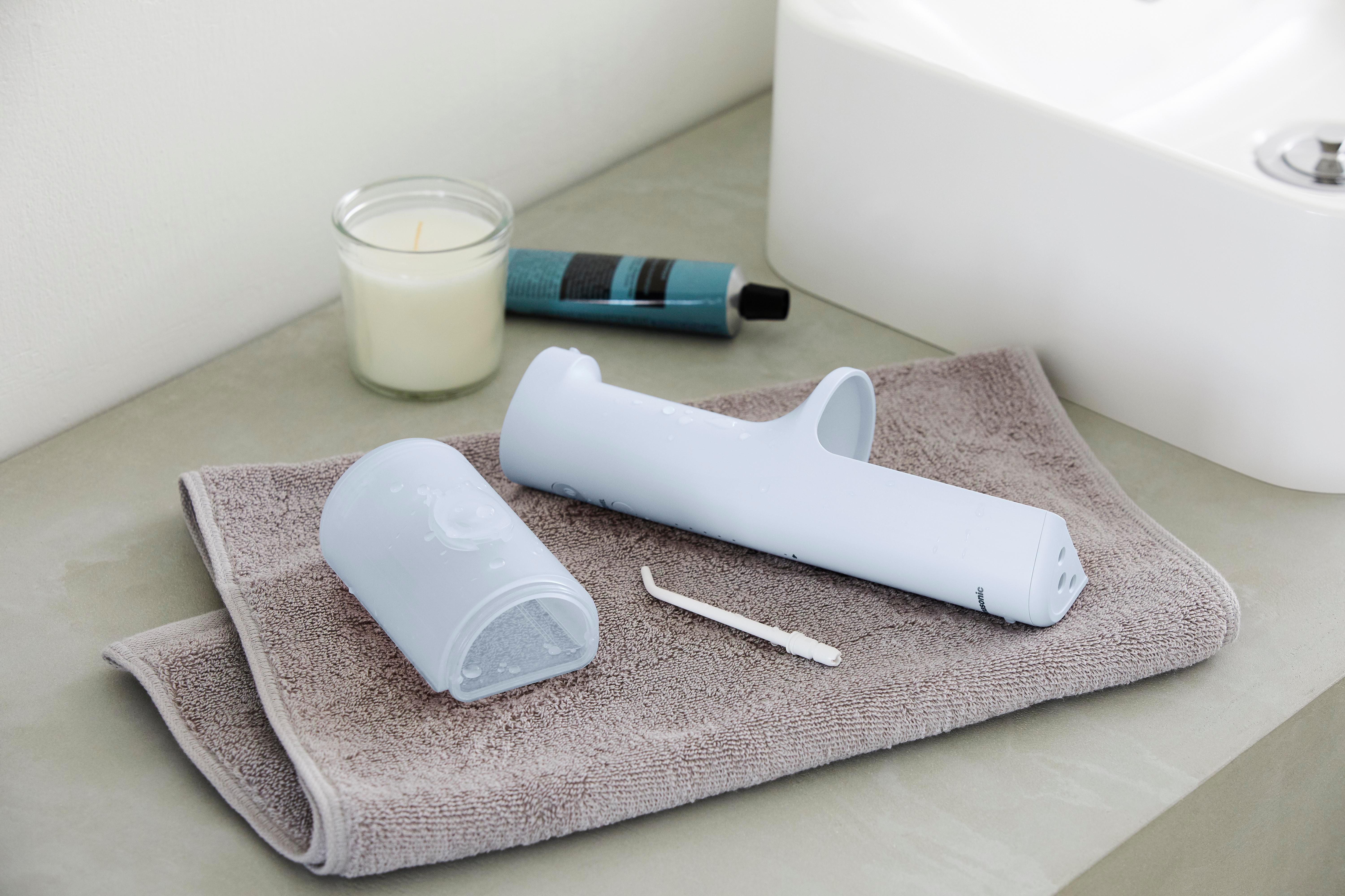 Zahnhygieneprodukte: Munddusche, Bürste, Zahnpasta, Kerze, auf einem grauen Handtuch.
