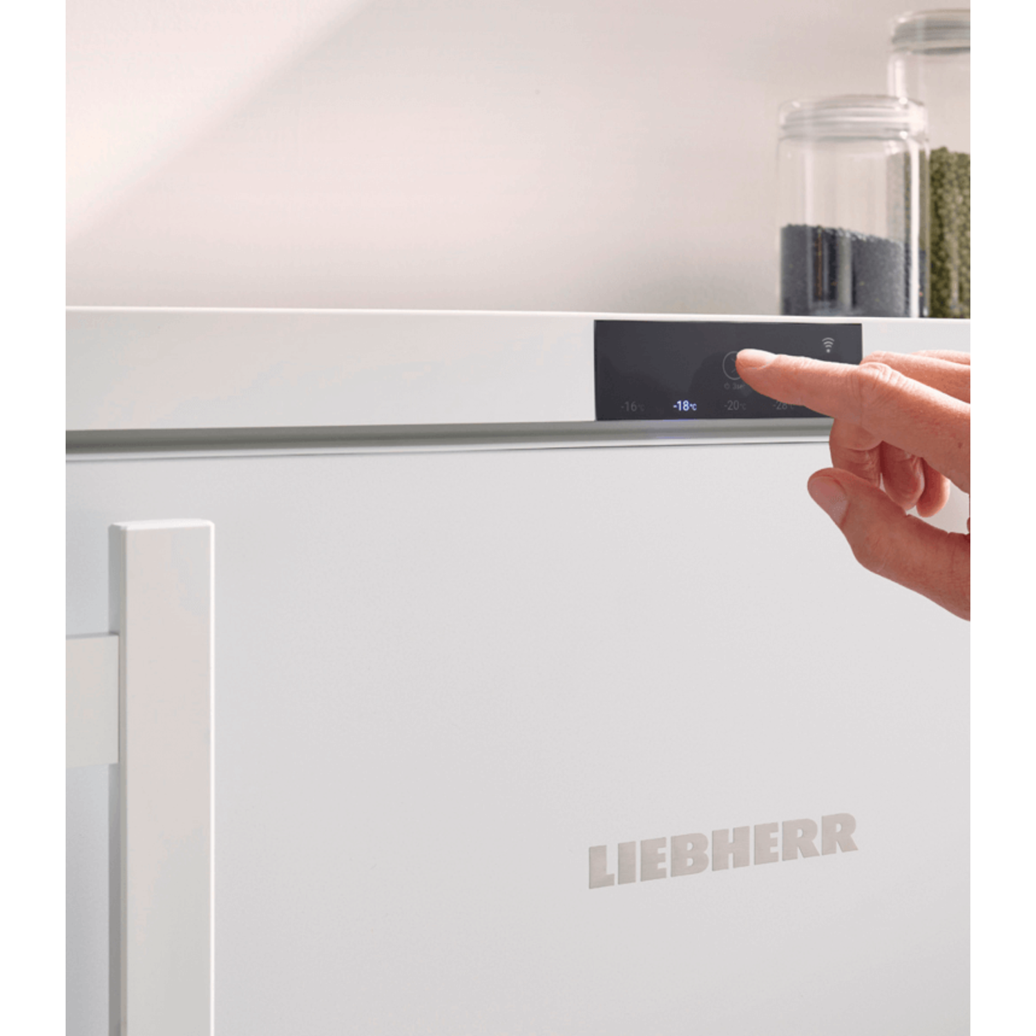 A hand is pressing a button on a white refrigerator. The freezer shows -18 degrees.