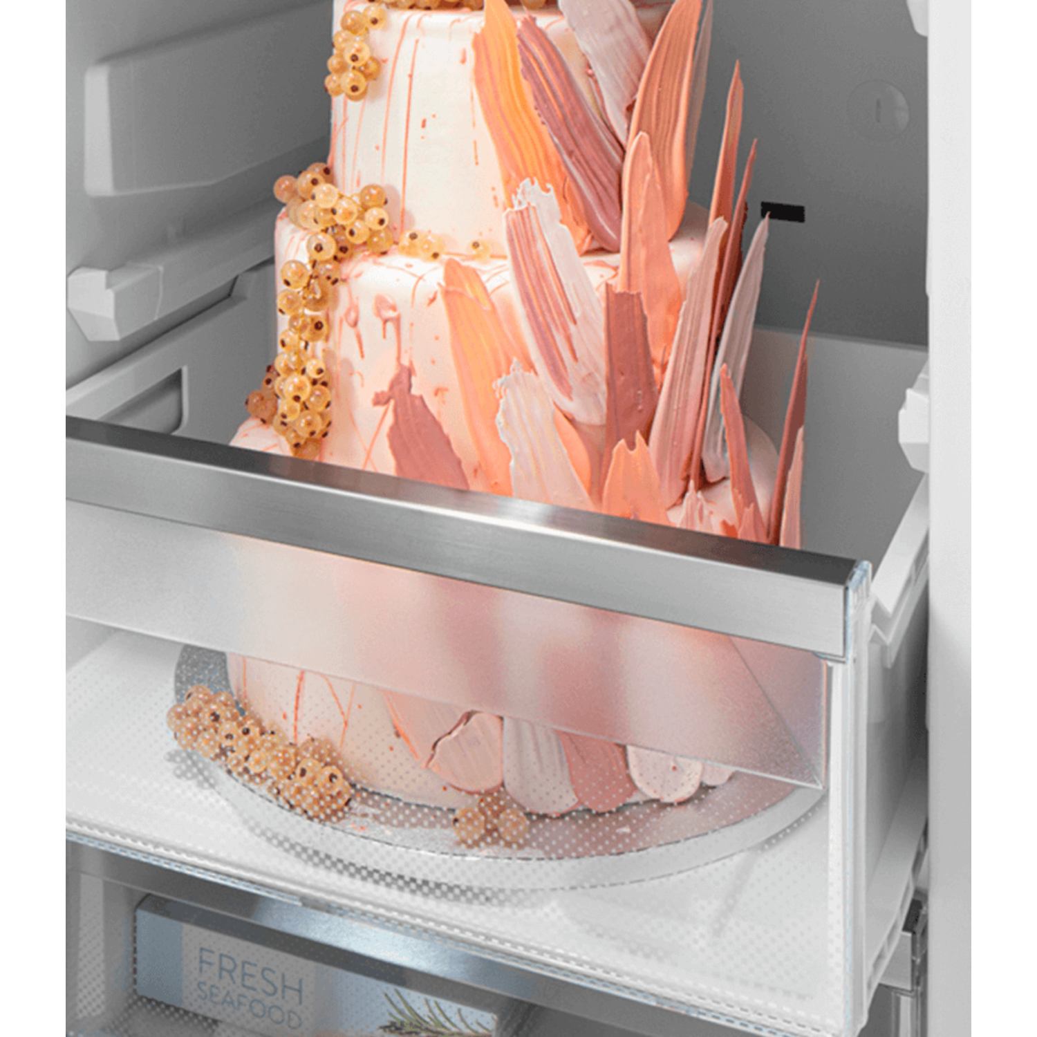 Cake inside a refrigerator. Two tiers, decorated with pink and white elements.