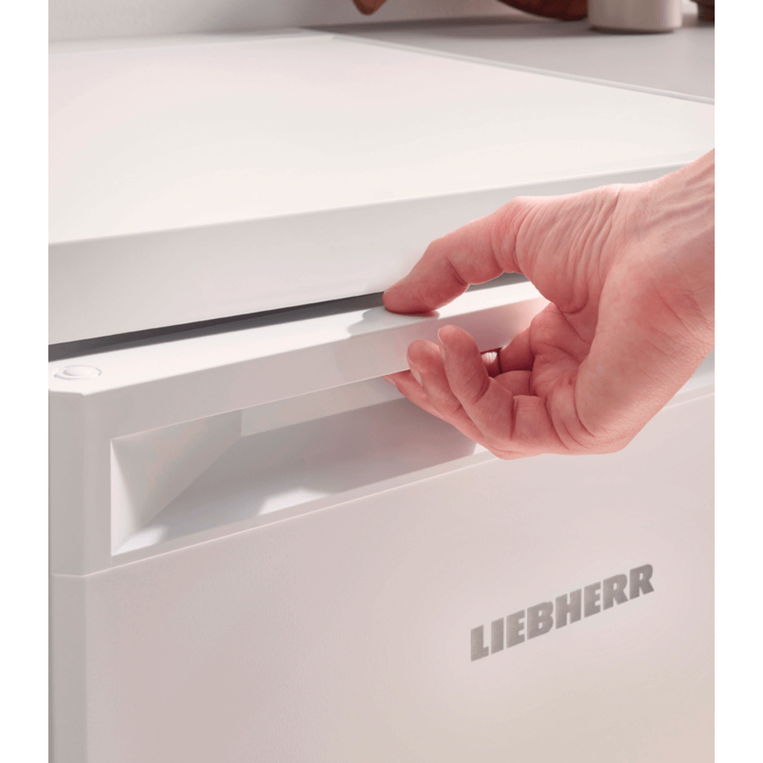 Hand opening a white refrigerator drawer. The brand name 'LIEBHERR' is visible.