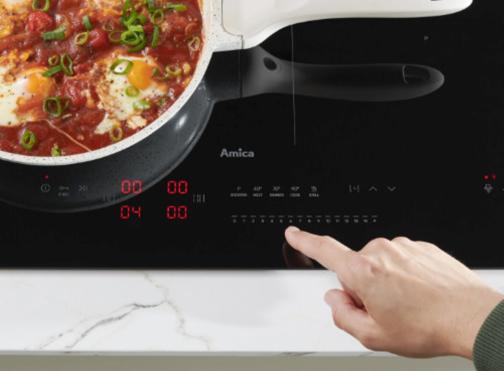 Płyta indukcyjna z dłonią dotykającą panelu sterowania, patelnia z jedzeniem.