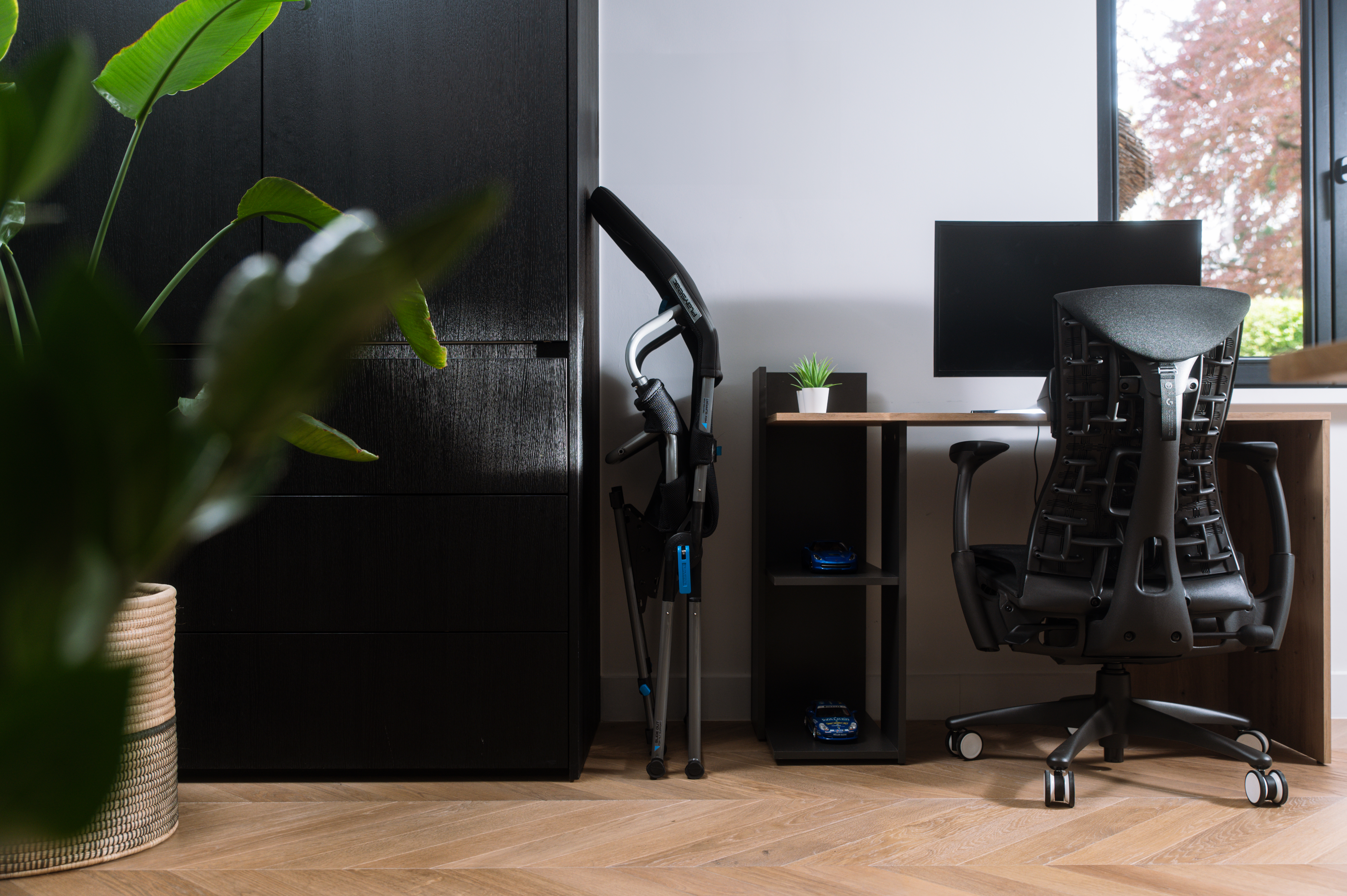 Büro-Setting mit Schreibtisch, Stuhl und Zubehör. Pflanze und Fenster im Hintergrund.