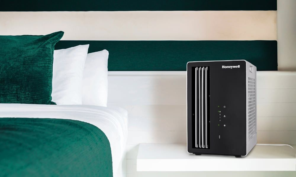 Czarny klimatyzator Honeywell na białym stoliku nocnym. Łóżko jest zielone.