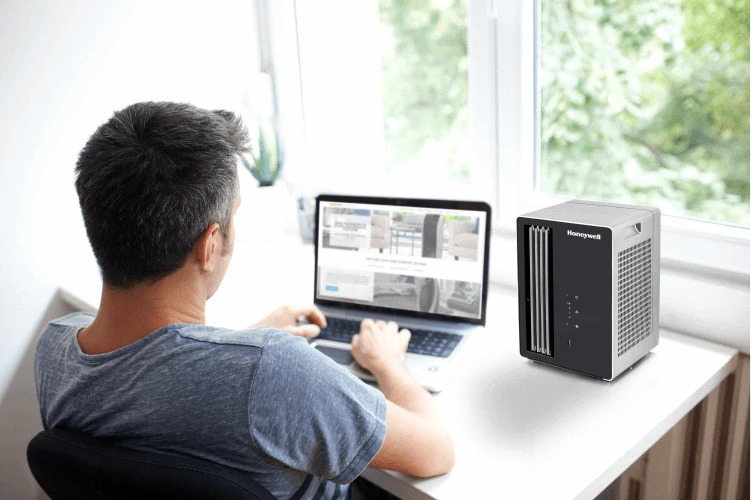 Mężczyzna używa laptopa obok oczyszczacza powietrza Honeywell.