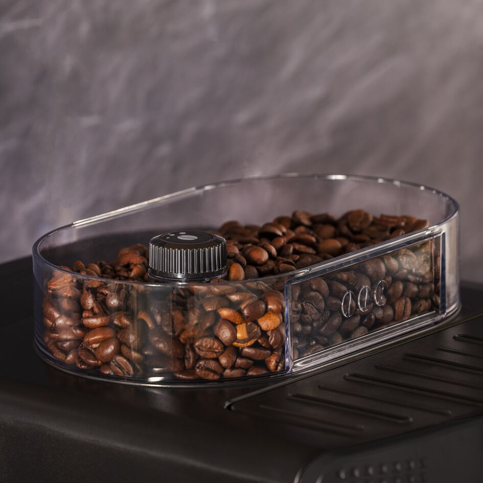 Récipient transparent à grains de café sur surface noire. Contient des grains torréfiés. Bouton noir dessus.