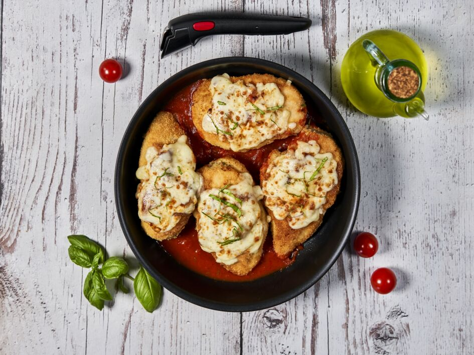 Overhead shot of four chicken parmesan portions in a black bowl with tomatoes.