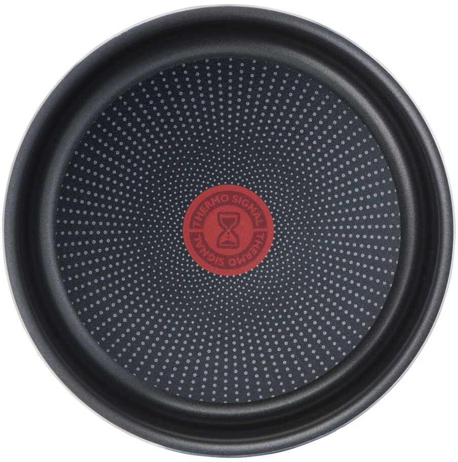 Close-up of a black frying pan bottom with red center logo and small white dots.