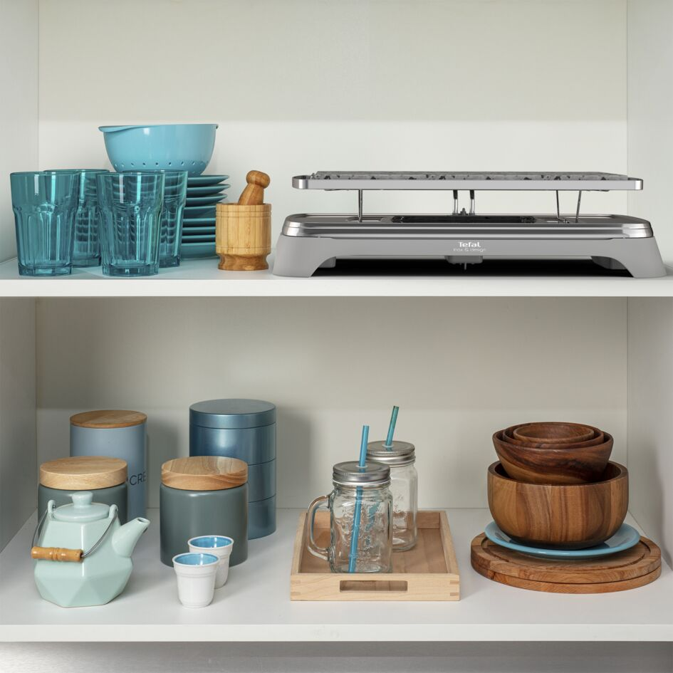 Keukenplanken met diverse items: glazen, kommen, theepotten en een raclette grill.