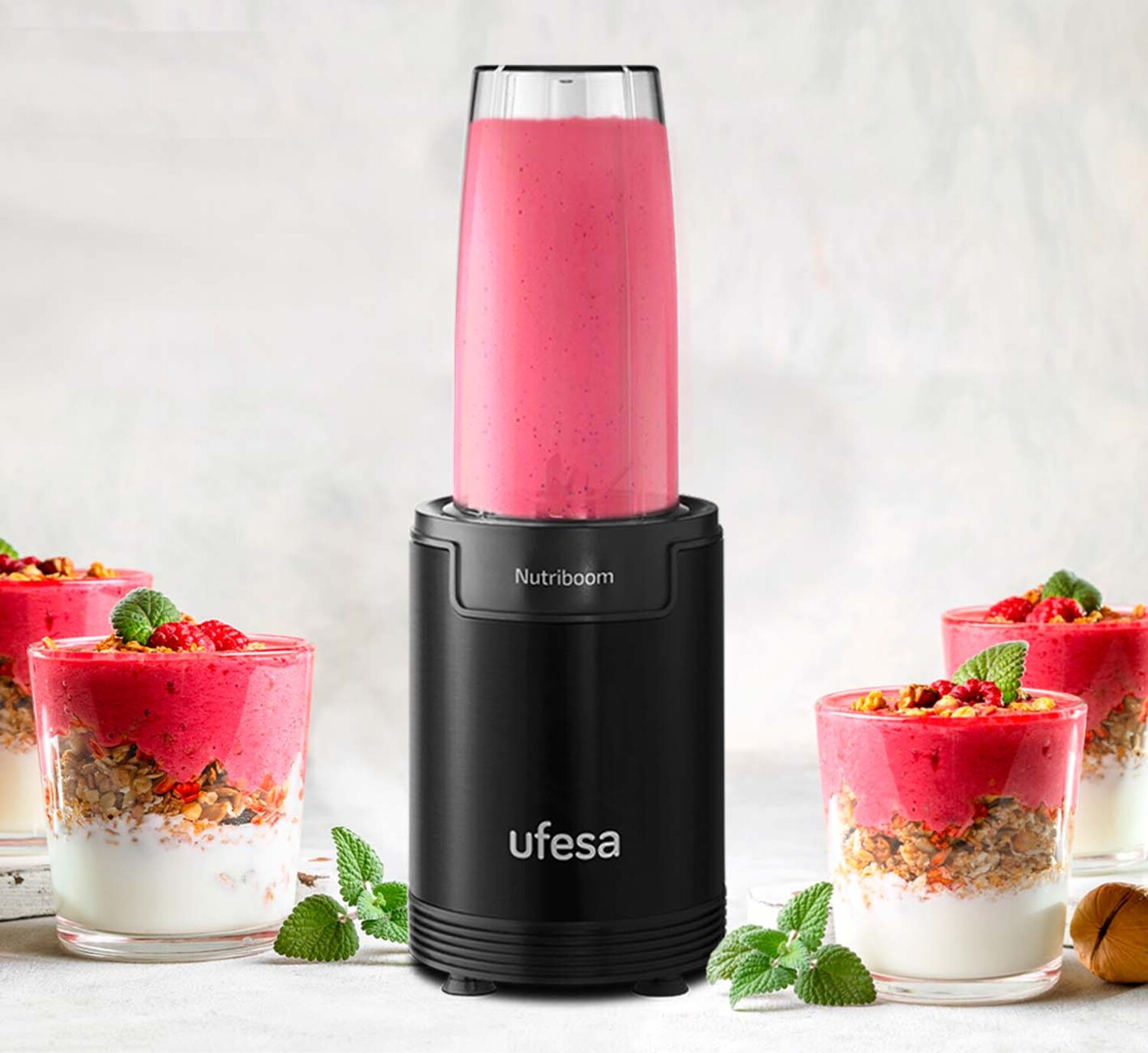 Una licuadora negra con un batido rosa. La licuadora está junto a cuatro vasos de batidos.
