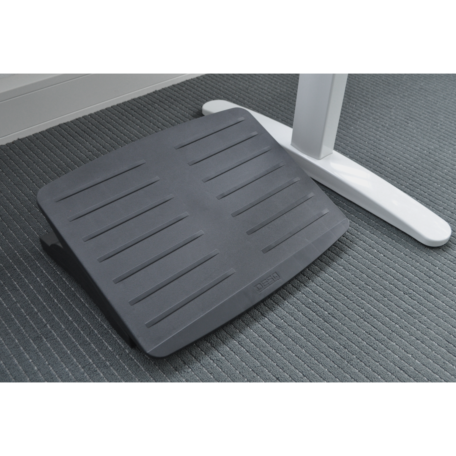 Gray footrest on a gray carpet. It's placed near a white desk leg.