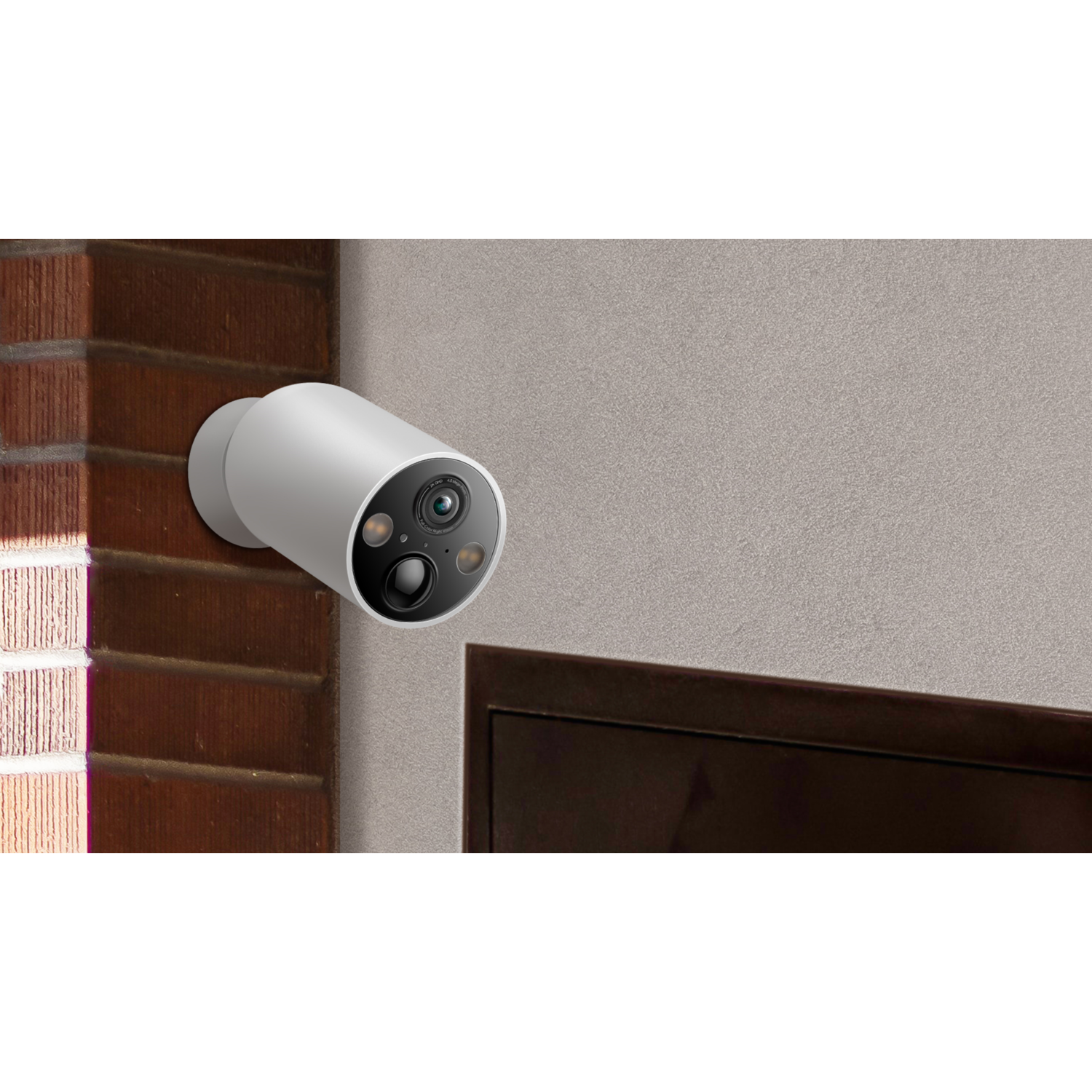 A white security camera mounted on a brick wall, with a gray wall in the background.