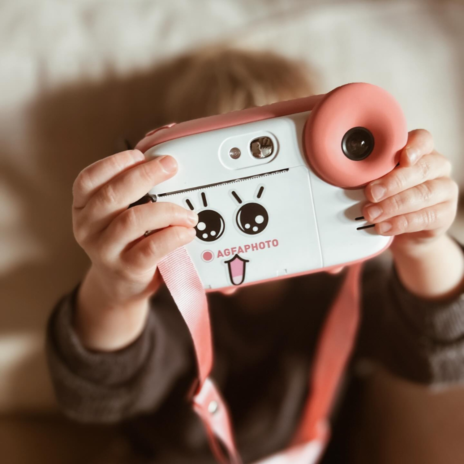 Child holding a pink and white camera with a cartoon face.