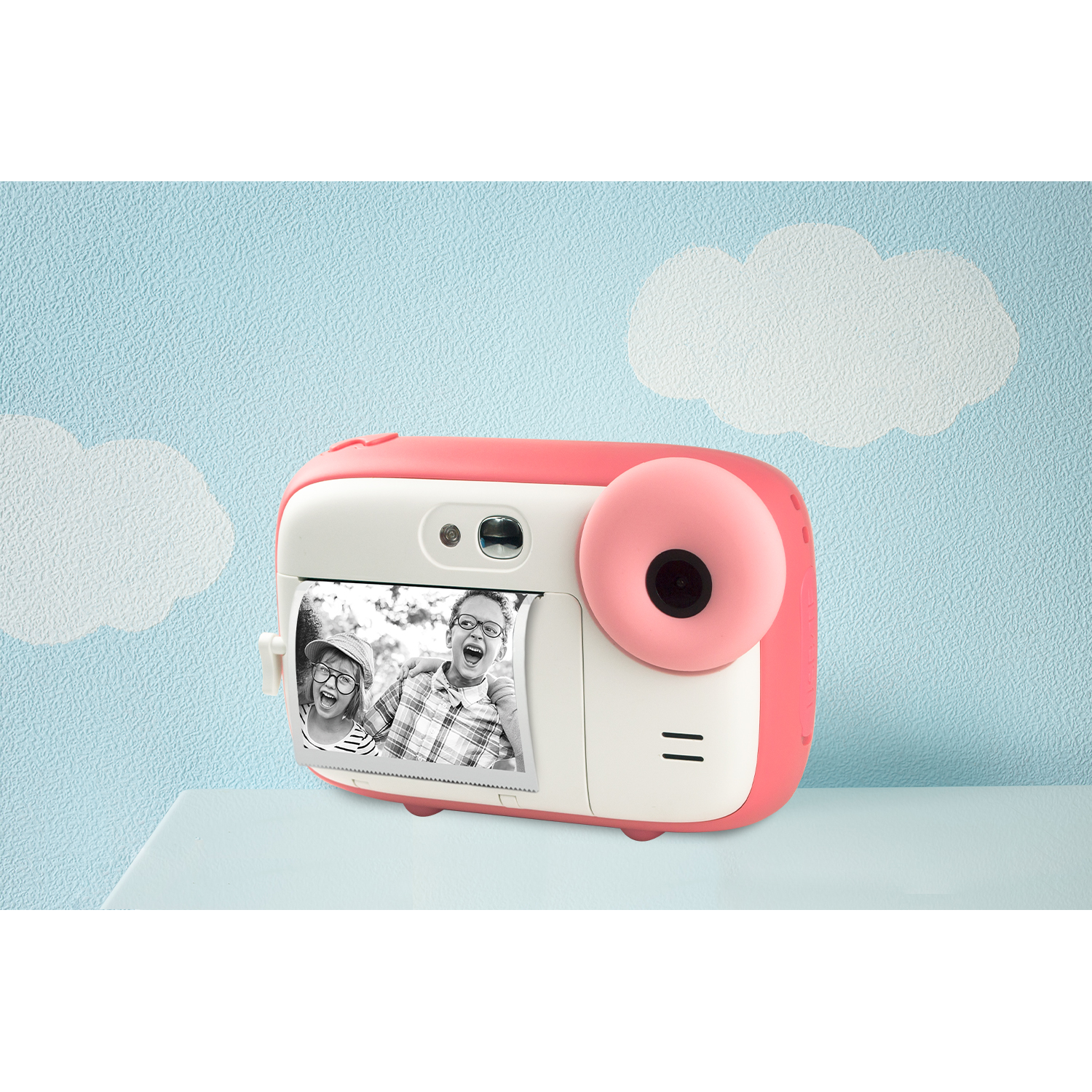 Pink and white instant camera with a photo of two kids. It's on a light blue table.