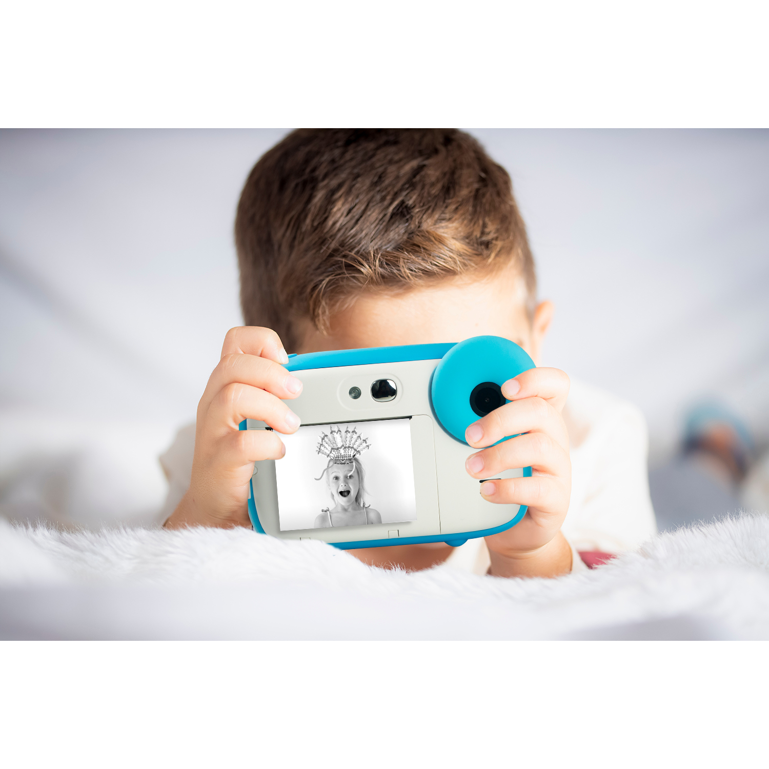 A child is taking a picture. The camera is blue and white, and the screen shows a photo.