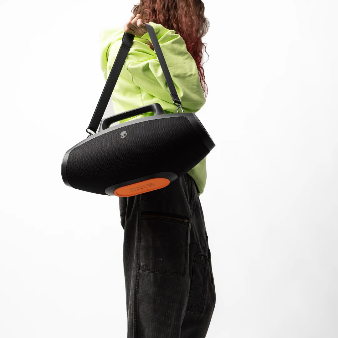 Une femme tient un haut-parleur noir avec une poignée et un détail orange.