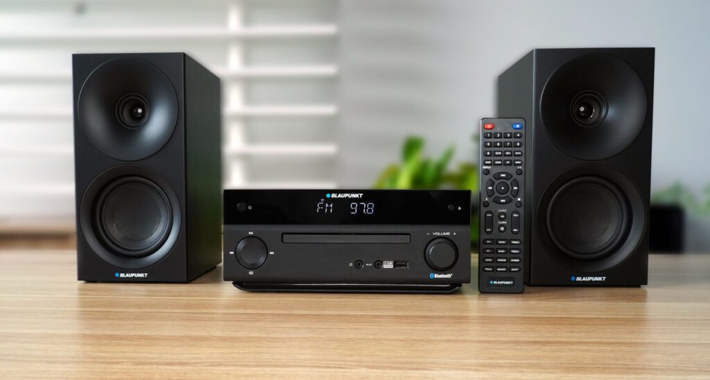 Czarny system stereo z dwoma głośnikami, odbiornikiem i pilotem na drewnianej powierzchni.