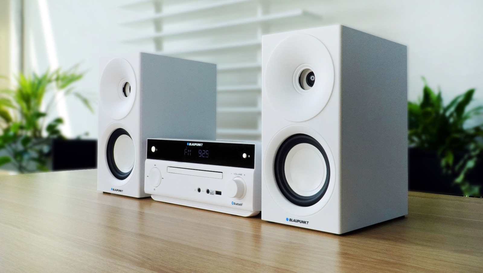 Biały zestaw stereo z dwoma głośnikami i jednostką centralną na drewnianym stole.