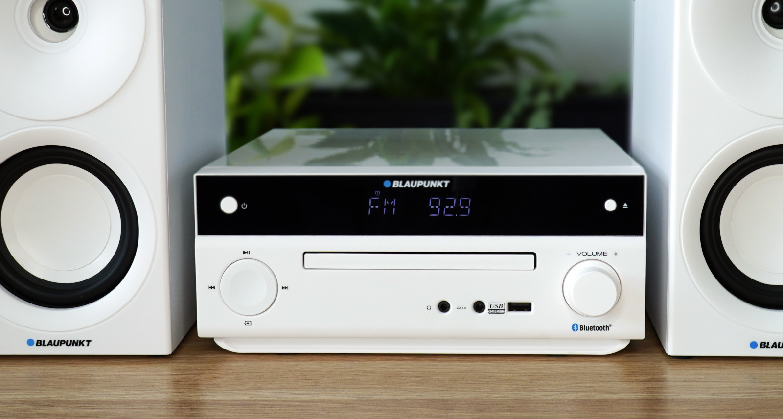 Biały zestaw stereo z cyfrowym wyświetlaczem, otoczony dwoma białymi głośnikami.