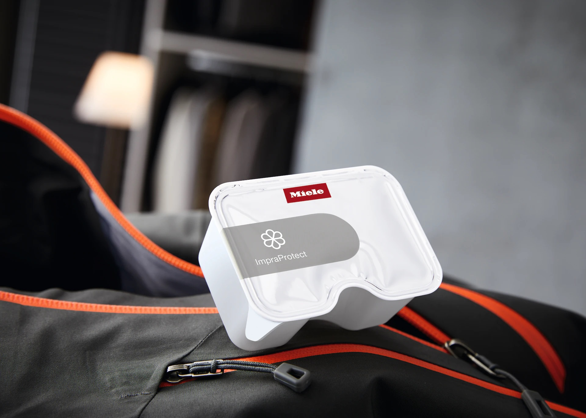 Otwarty pojemnik na chusteczki Miele ImraProtect na szarej torbie, w szafie z lampą.