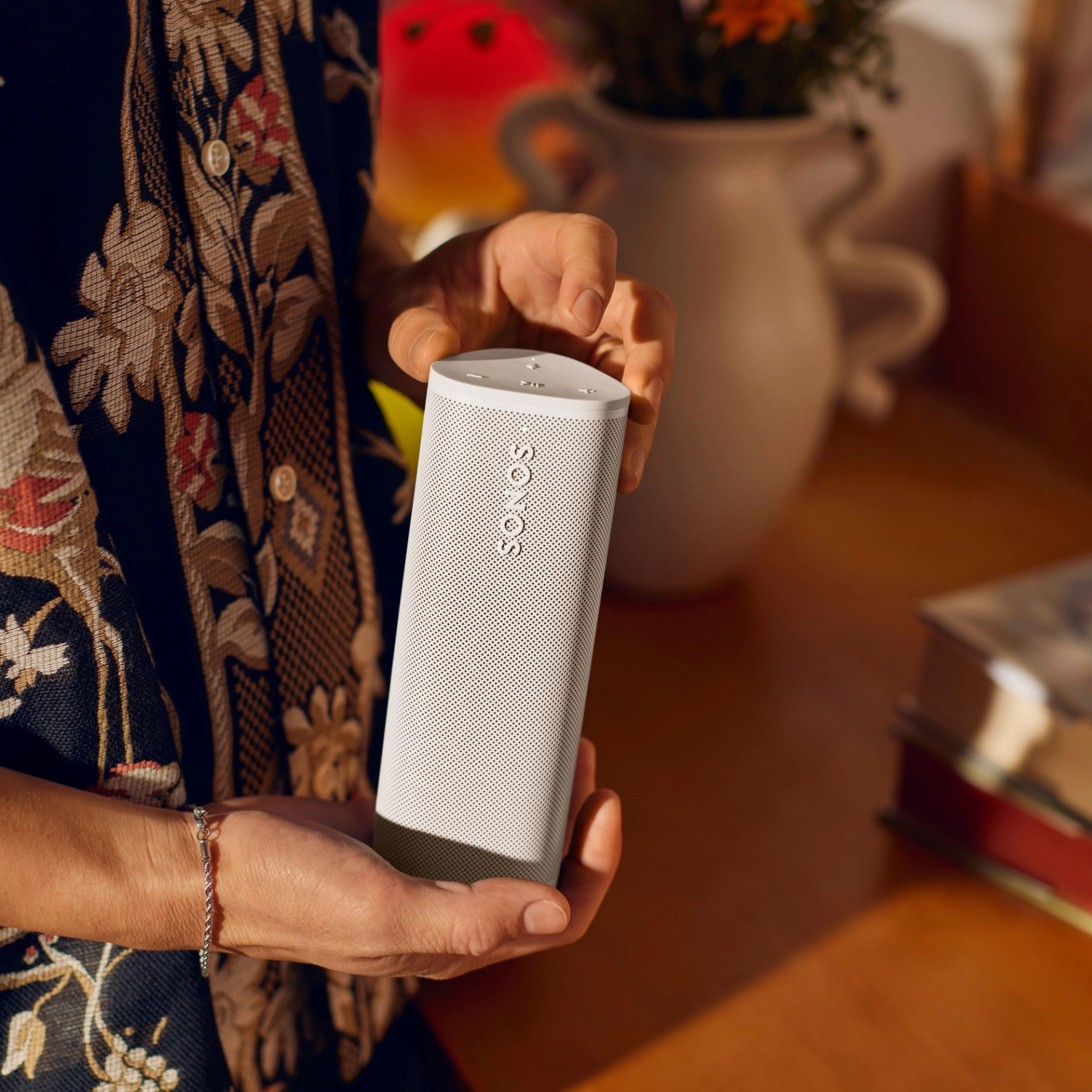 Une personne tenant une enceinte Sonos blanche, mains posées sur une table en bois.