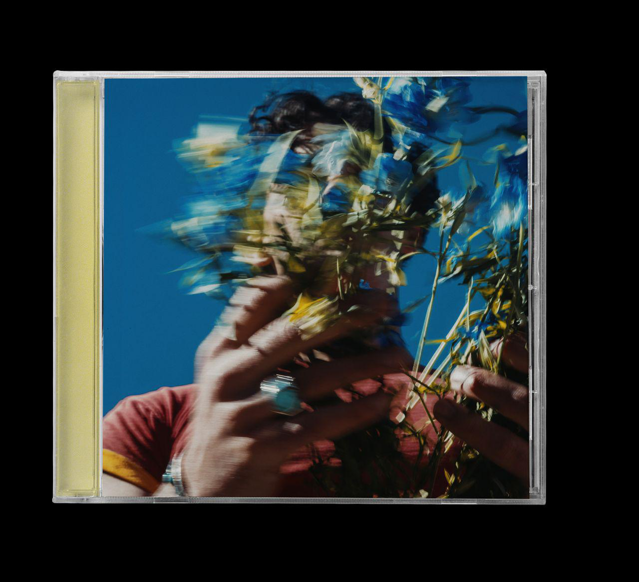 Eine Person, die einen Strauß blauer Blumen hält und ihr Gesicht verdeckt, vor einem blauen Himmelshintergrund.