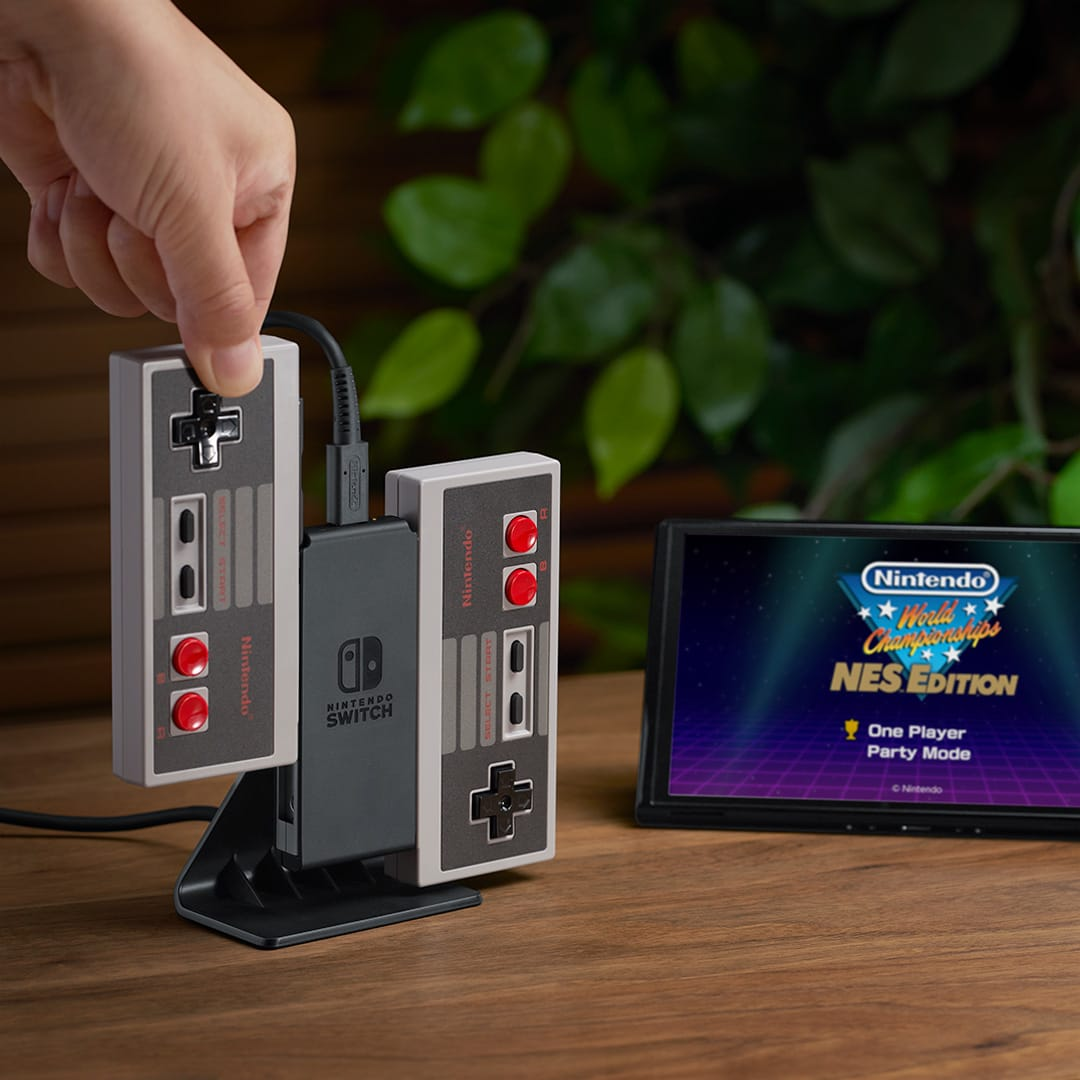 Eine Person hält zwei Nintendo-Controller, die mit einer grauen Nintendo Switch-Konsole verbunden sind. Ein Bildschirm ist sichtbar.