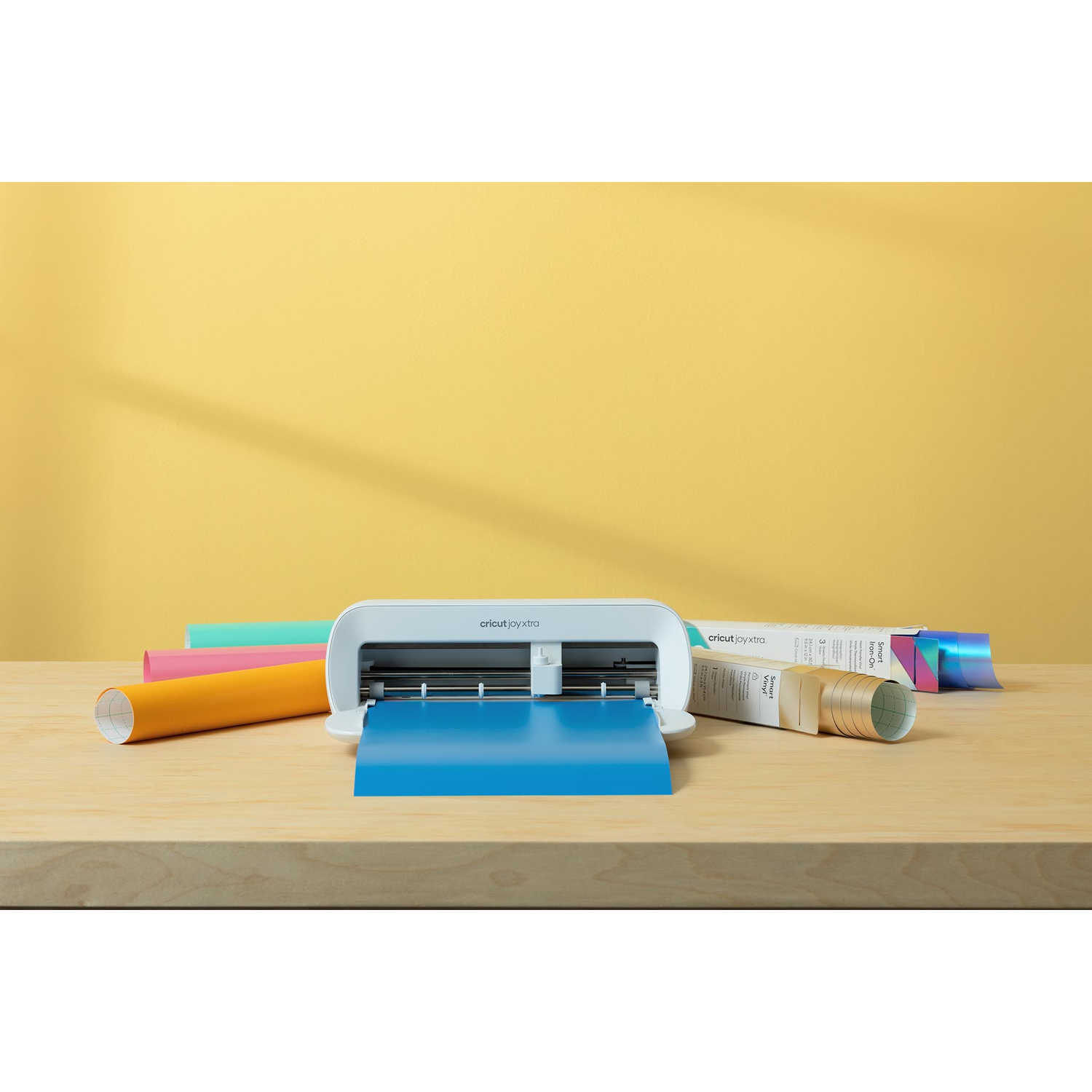 Een witte Cricut snijmachine met blauwe snijmat op een houten tafel.
