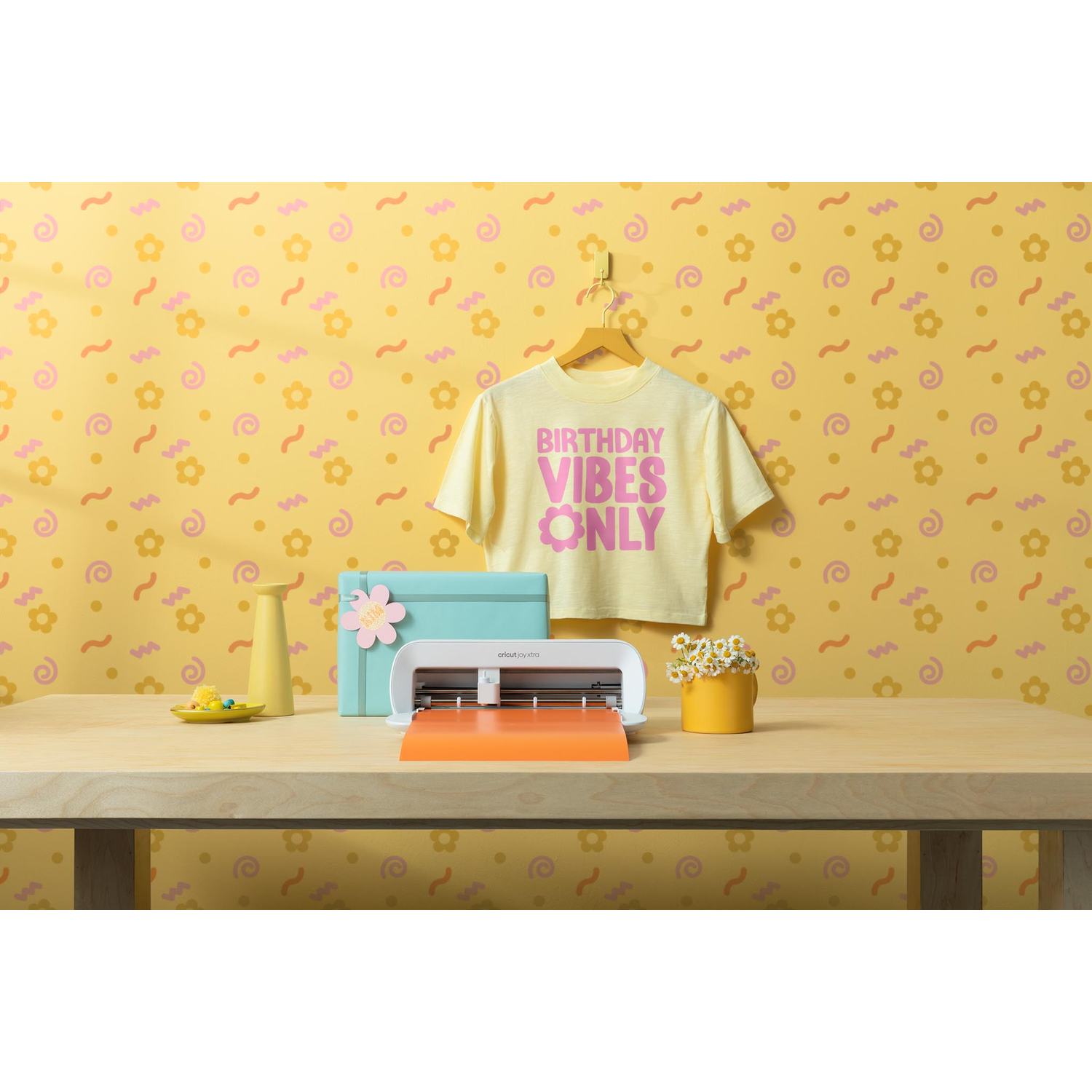 Een knutseltafel met een Cricut-machine, een t-shirt met 'Birthday Vibes Only' en een gele vaas.