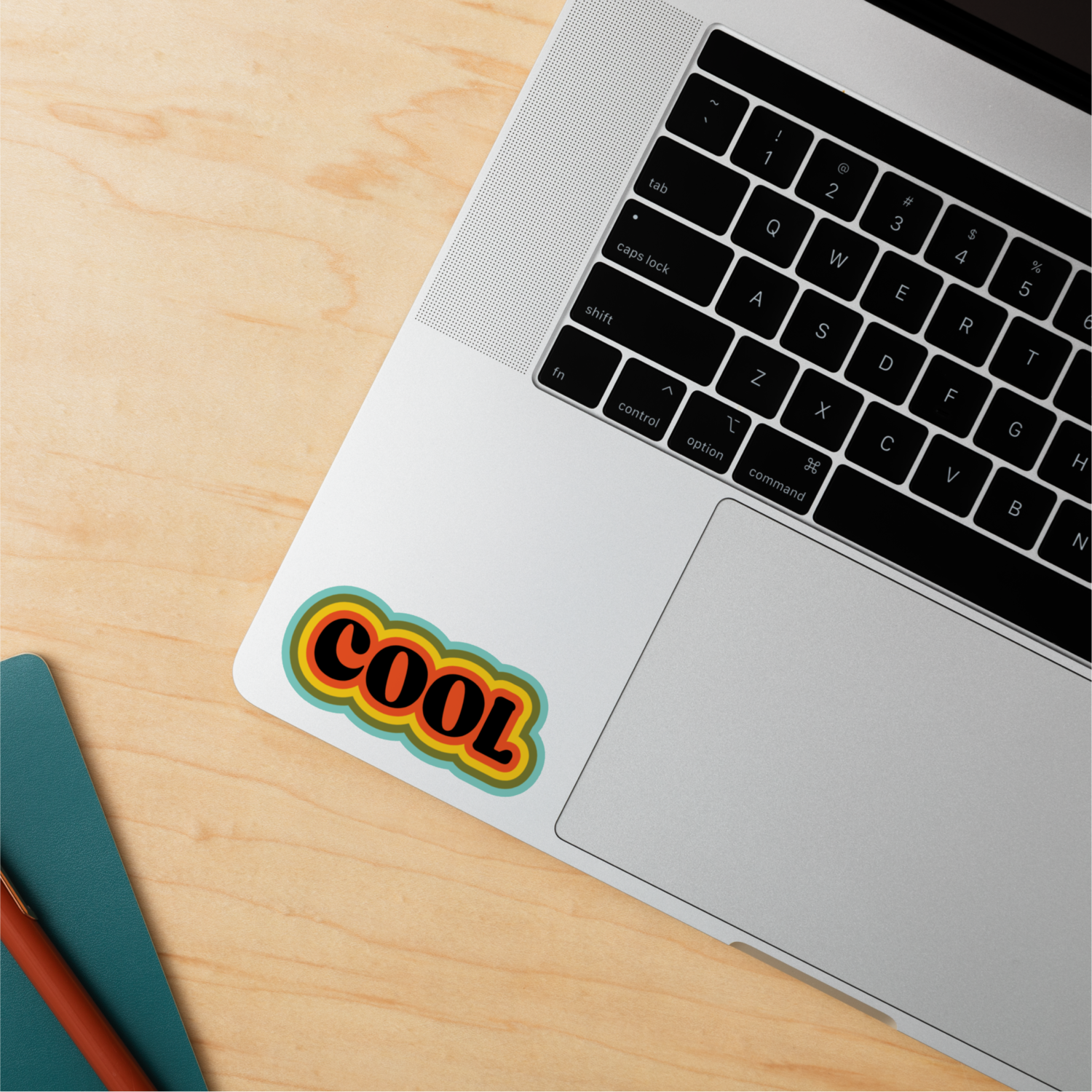 Laptoptoetsenbord met een kleurrijke 'COOL' sticker op de trackpad, op een houten oppervlak.