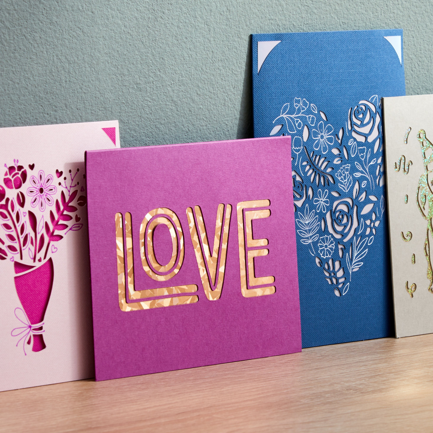 Four colorful greeting cards with cut-out designs, on a wooden surface.