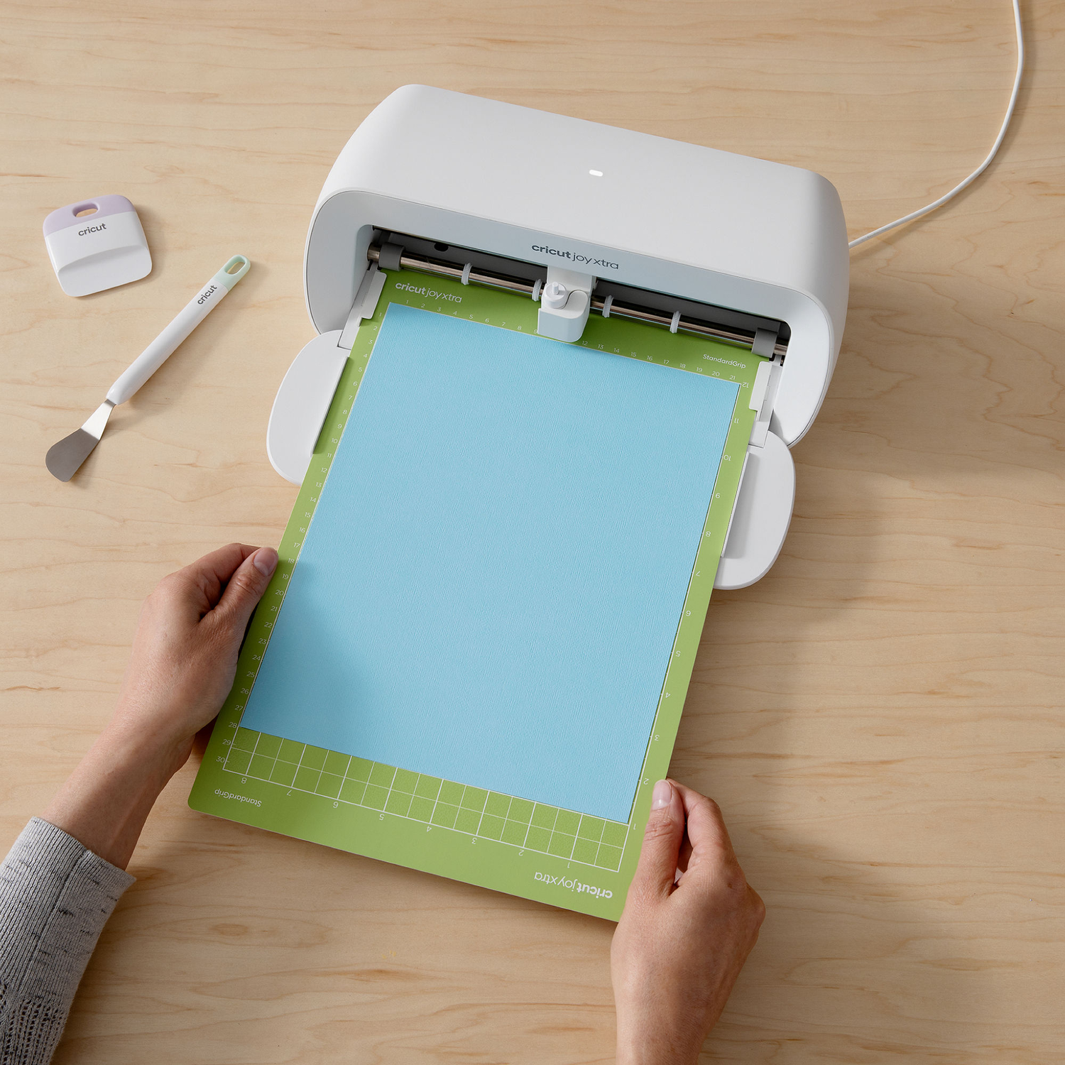 Persoon die een Cricut-machine gebruikt. Groene mat met papier, gereedschap ernaast.