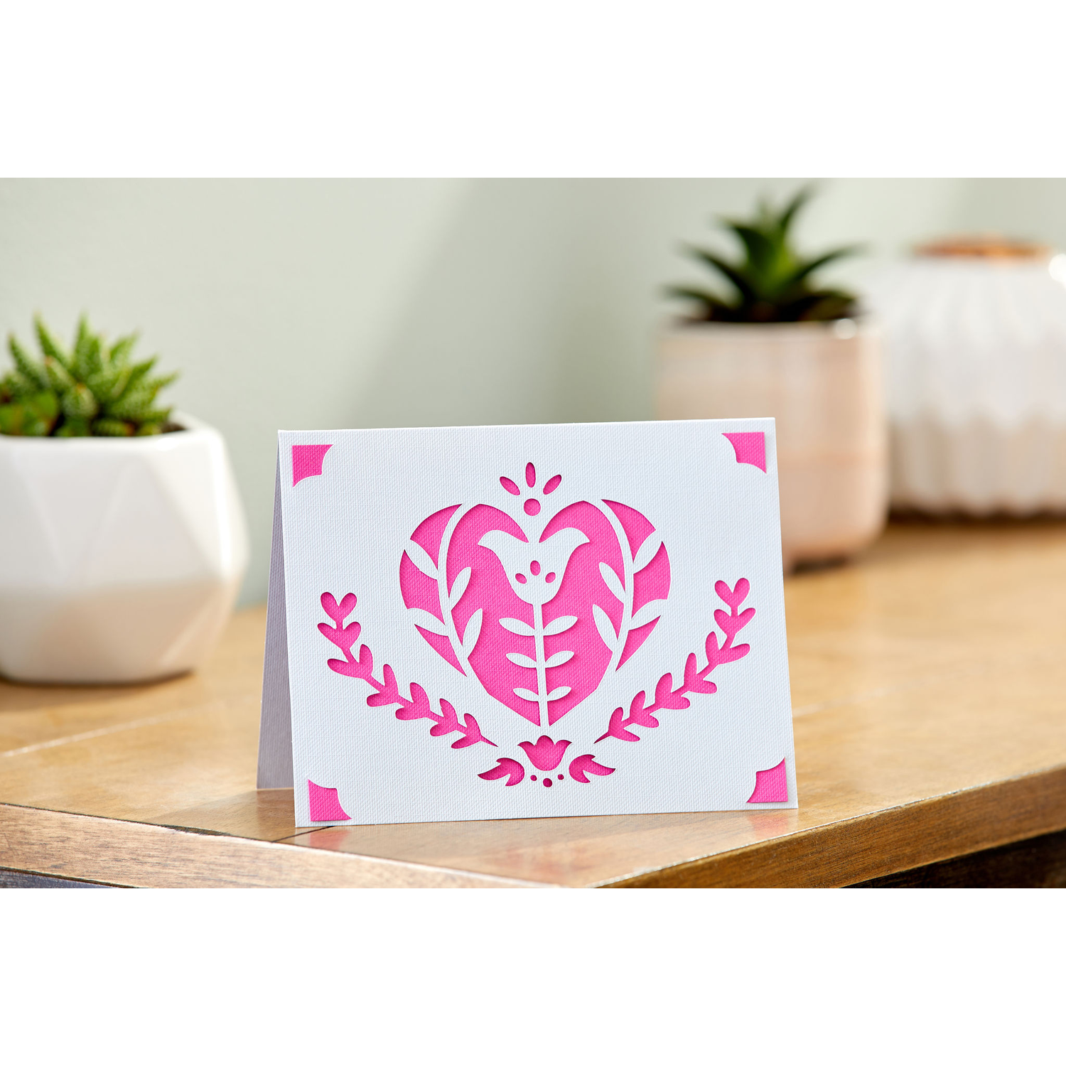 Wenskaart met hart- en bloemenontwerp. Roze hart uitgesneden op witte kaart. Houten tafel achtergrond.