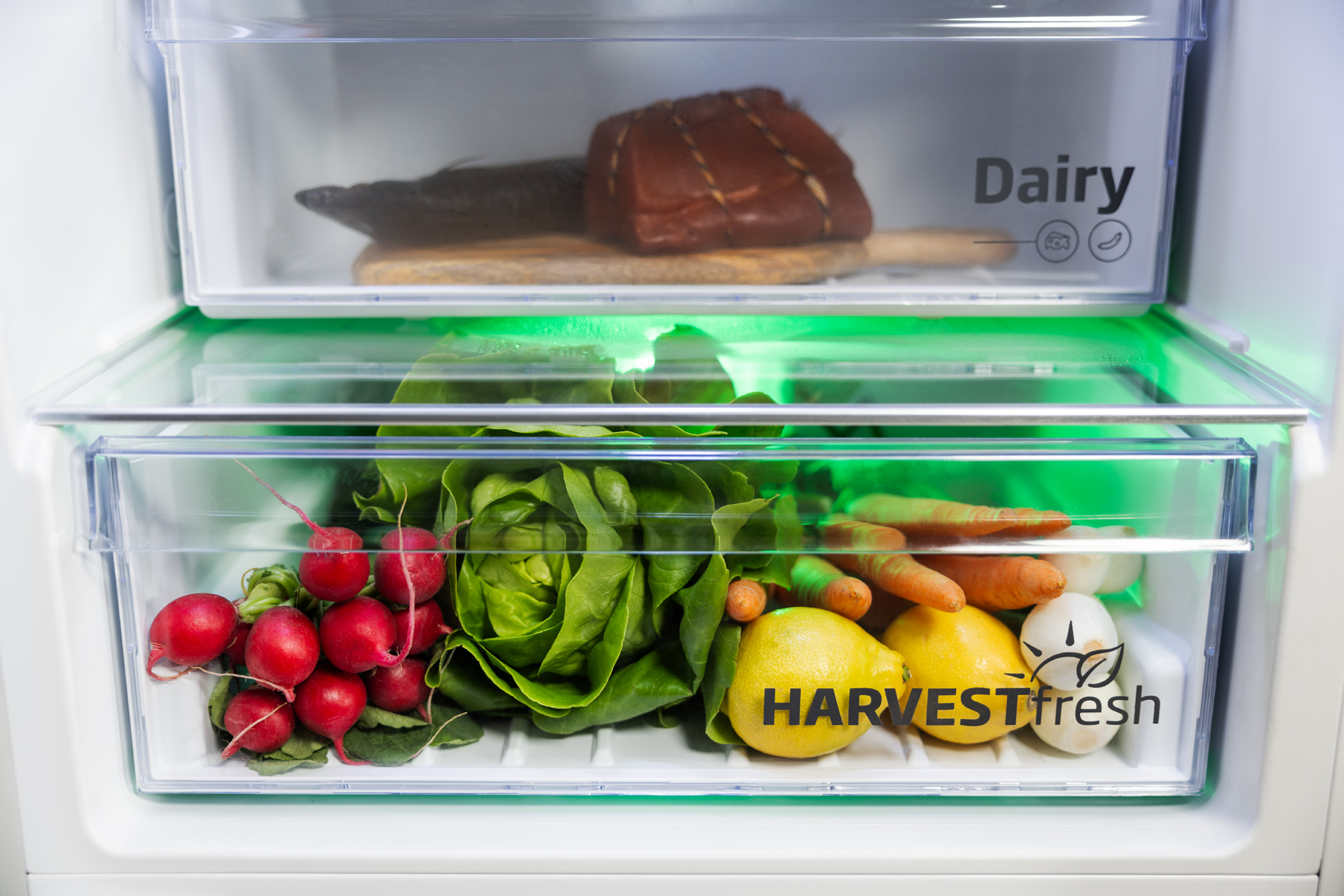 Wewnątrz lodówki: górna półka z mięsem i dolna półka z warzywami, takimi jak rzodkiewki, marchew i sałata.