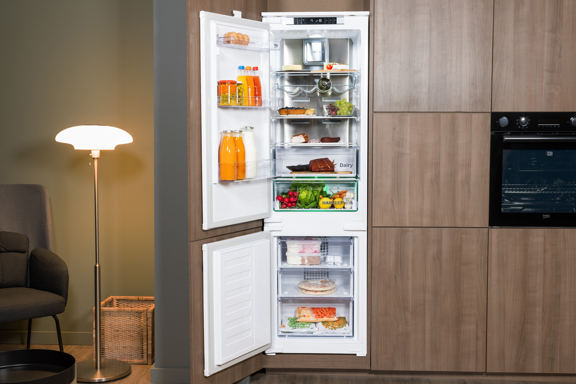 Otwarta lodówka wypełniona jedzeniem. Zamrażarka jest otwarta. Tło kuchenne.